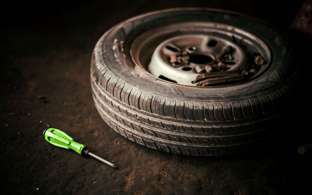 A wheel off the car with its nuts and a tool laid beside it