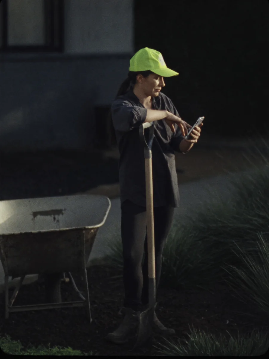 Sample photo: a landscaper in a hi-vis cap leans on a spade and checks her phone