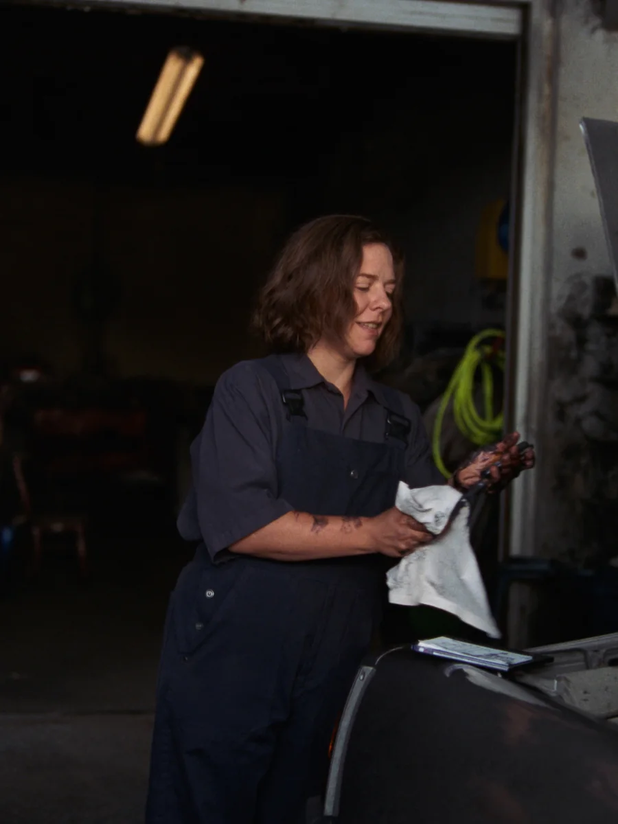 Sample photo: a mechanic in overalls wipes grease from her hands beside an open bonnet