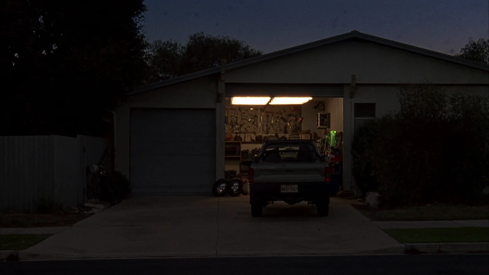 Sample photo: a small suburban workshop at dusk, roller door open and a ute parked out front